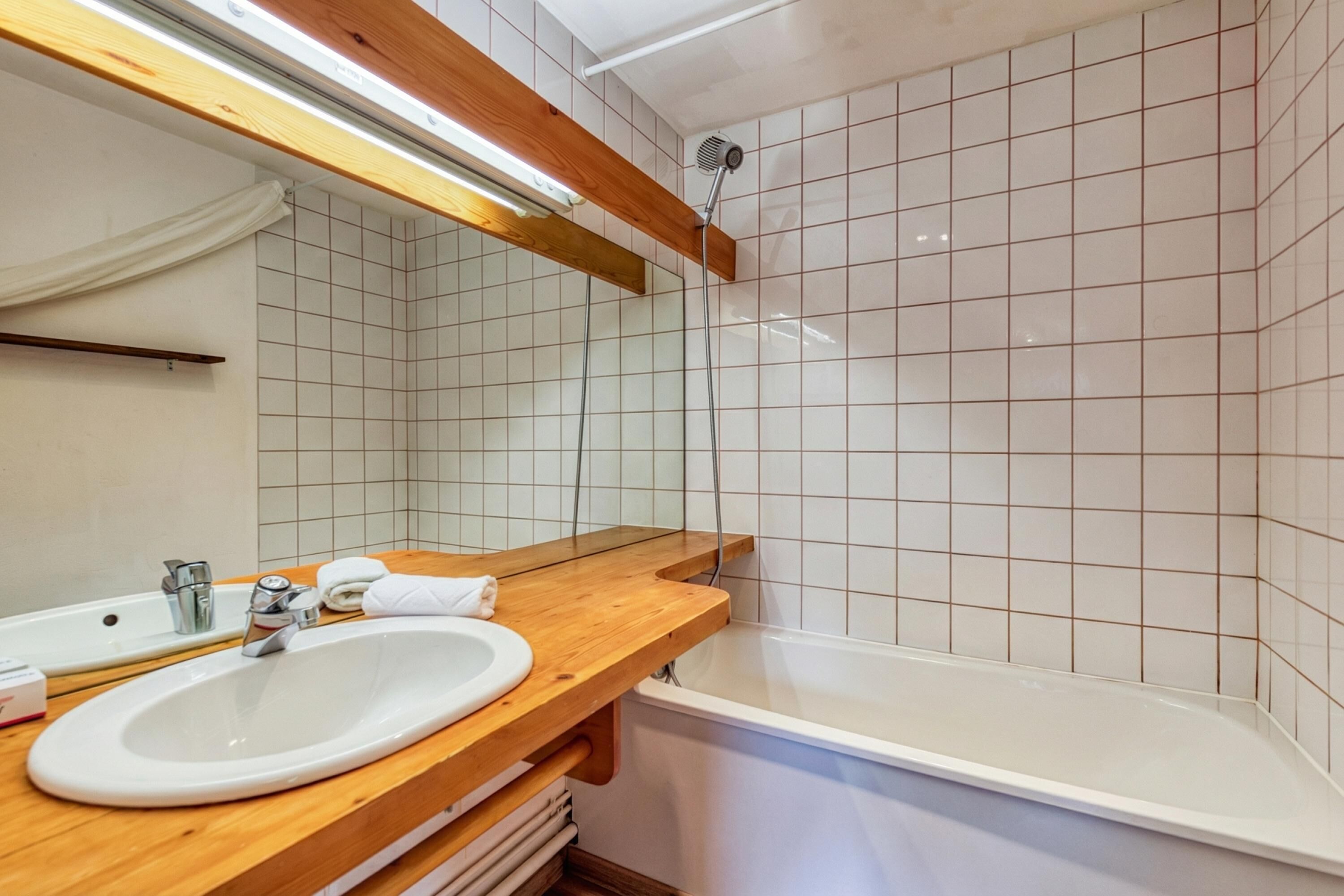 Un baño con tocador de madera, lavamanos blanco, espejo y bañera blanca.
