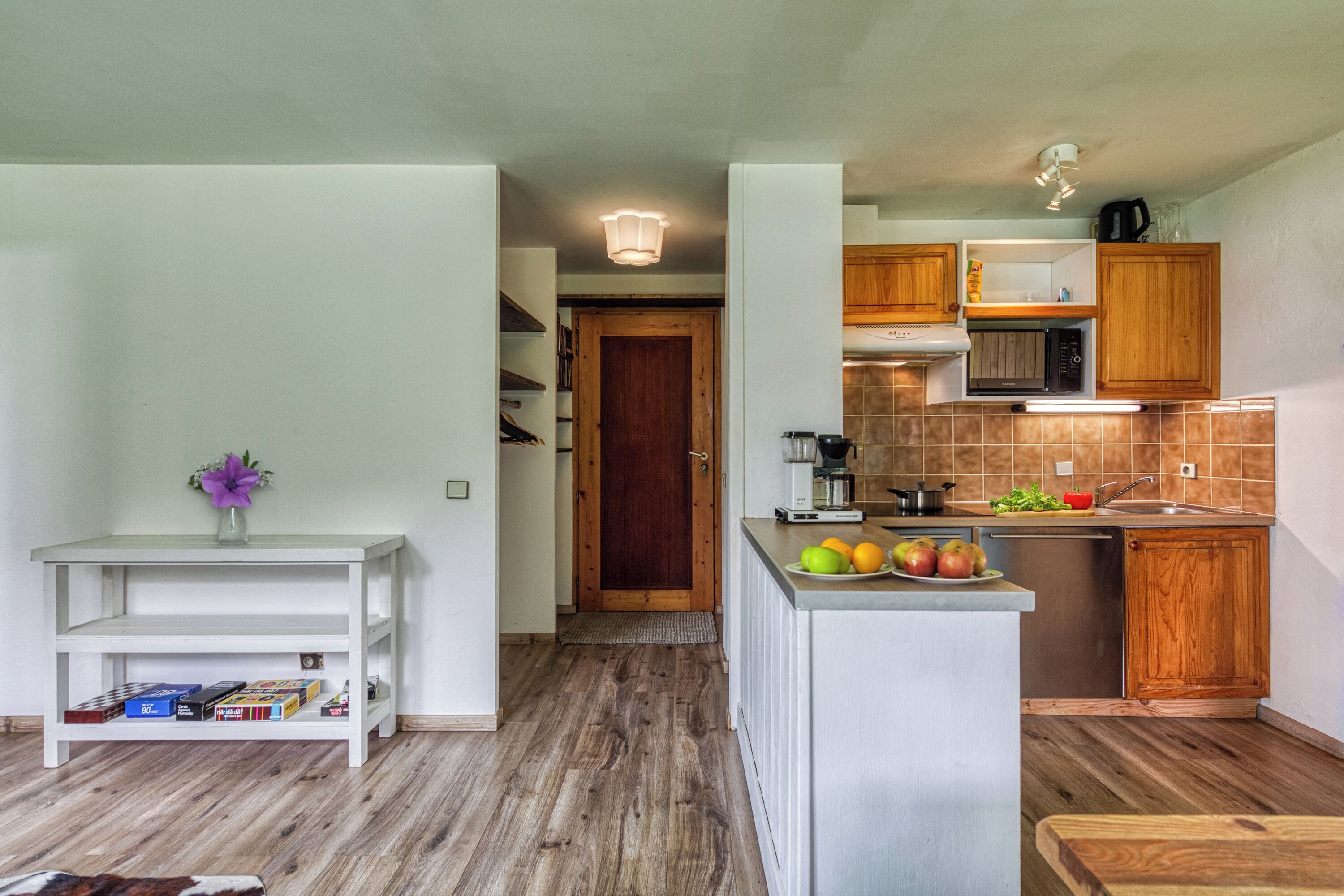 A modern kitchen with wooden cabinets, a built-in microwave, and a sink. There is a small island with fruits and a coffee maker.