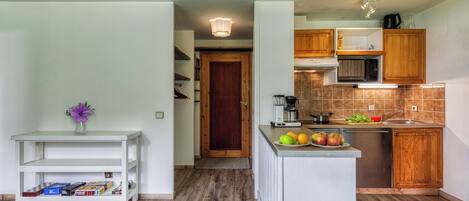 Une cuisine moderne avec des meubles en bois, un four à micro-ondes encastré et un évier. On y trouve un petit îlot central avec des fruits et une machine à café.