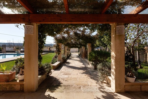 A stone pathway leading to a pool under a pergola with columns and potted plants.