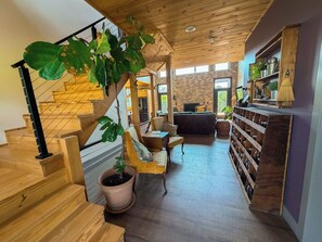 Una escalera de madera con una planta, un rincón de descanso con una mesa y sillas, y una estantería con frascos.