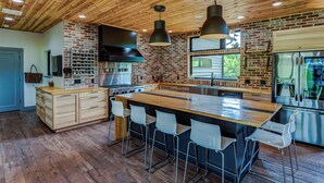 Una cocina moderna con una isla grande, taburetes de bar, pared de ladrillo y electrodomésticos de acero inoxidable.