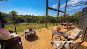 A wooden deck with outdoor furniture, a table with flowers, and a view of a green landscape. - 7-Bedroom: Hoops, Pickleball, Movies, Books & Games!  (Weston)