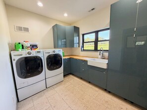 A laundry room with two front-loading washing machines, a sink, and a window with a view of the outdoors.