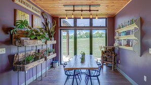 Un comedor con una mesa y sillas de madera, rodeado de plantas en macetas y estantes con frascos.