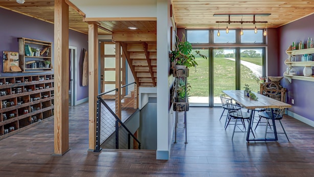 Una habitación amplia con una escalera de madera, un comedor con mesa y sillas, y un gran ventanal que ofrece vistas al exterior.