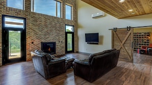 Amplia sala de estar con pared de ladrillo, sofás de cuero, chimenea, televisor y una puerta corrediza de estilo rústico que da a una bodega de vinos.