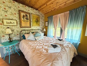 Ein Schlafzimmer mit einem Bett, einem Nachttisch, einer Lampe und einem Fenster mit Vorhängen.