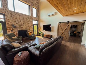 Ein geräumiges Wohnzimmer mit Backsteinwand, einem großen Ledersofa, einem Flachbildfernseher und einer Schiebetür im Scheunenstil.