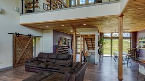Un amplio salón con un sofá de cuero grande, piso de madera y vistas al exterior.