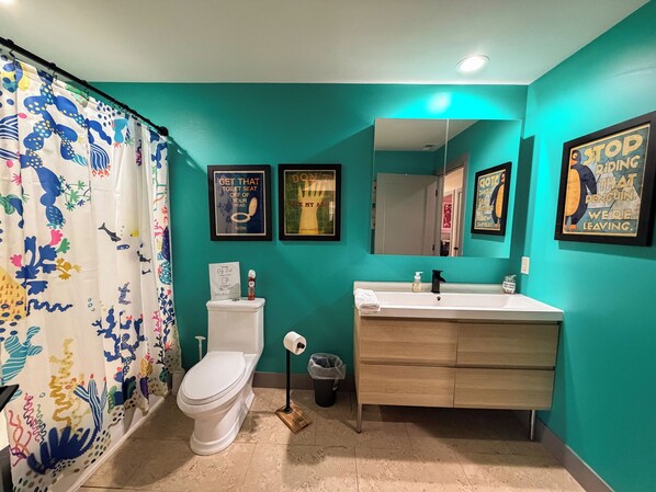 Un baño con inodoro, lavamanos y cortina de ducha. Hay tres cuadros en la pared.