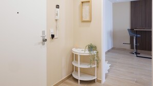 Ein Zimmer mit einer weißen Tür, einem kleinen weißen Regal mit einer Pflanze, einem gerahmten Bild an der Wand und einem Holzboden.
