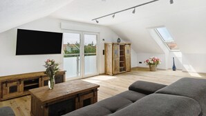 Un loft moderne doté d’un téléviseur à écran plat, de meubles en bois, d’un canapé et d’une lucarne.