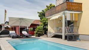 Une piscine avec des chaises longues, un patio couvert et un bâtiment doté d’un balcon.