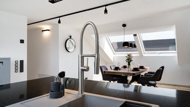 Une cuisine moderne dotée d’un évier en acier inoxydable, d’un coin repas avec une table et des chaises en bois, et d’une lucarne au plafond.