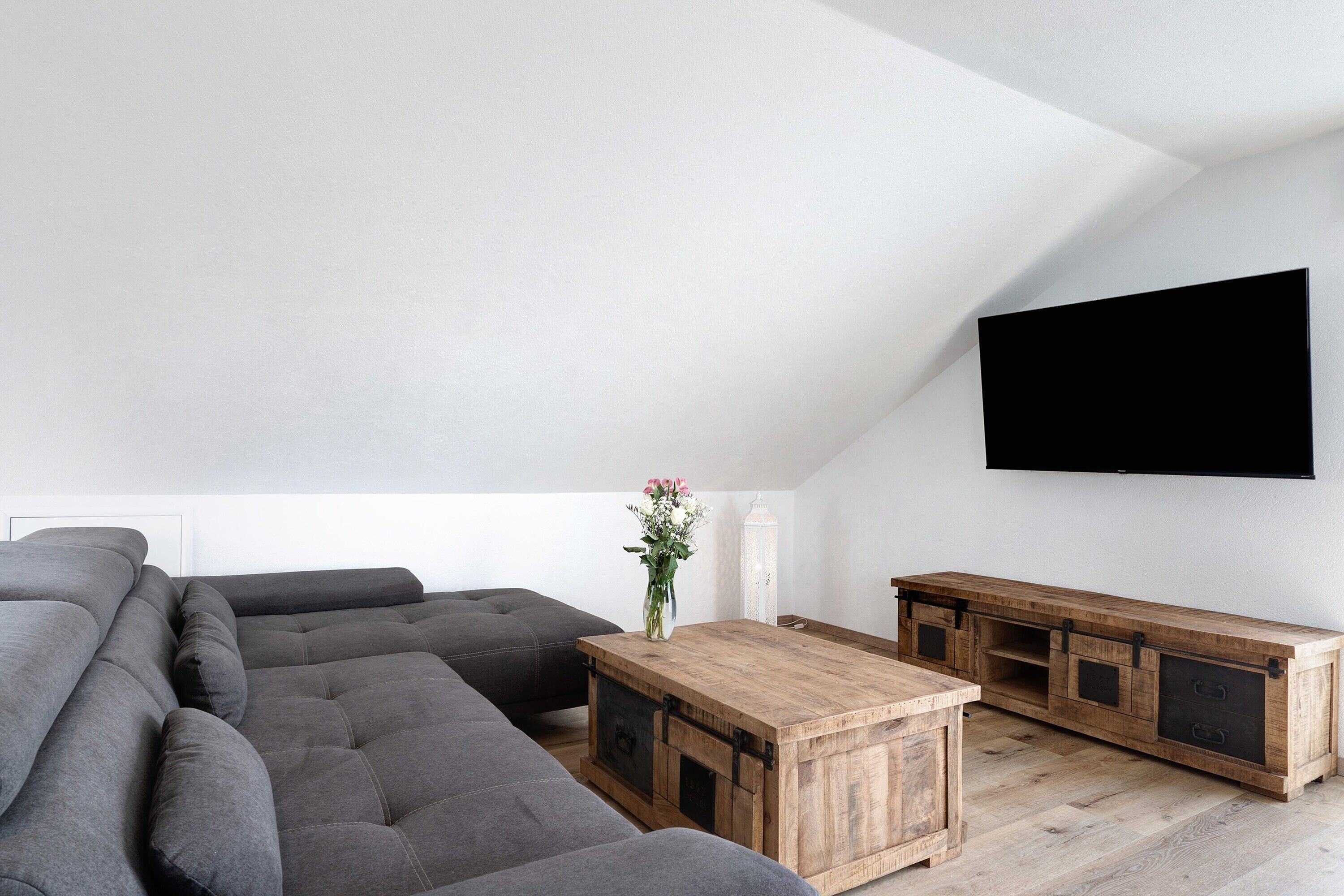 A modern living room with a sectional sofa, wooden coffee table, and a TV mounted on the wall.