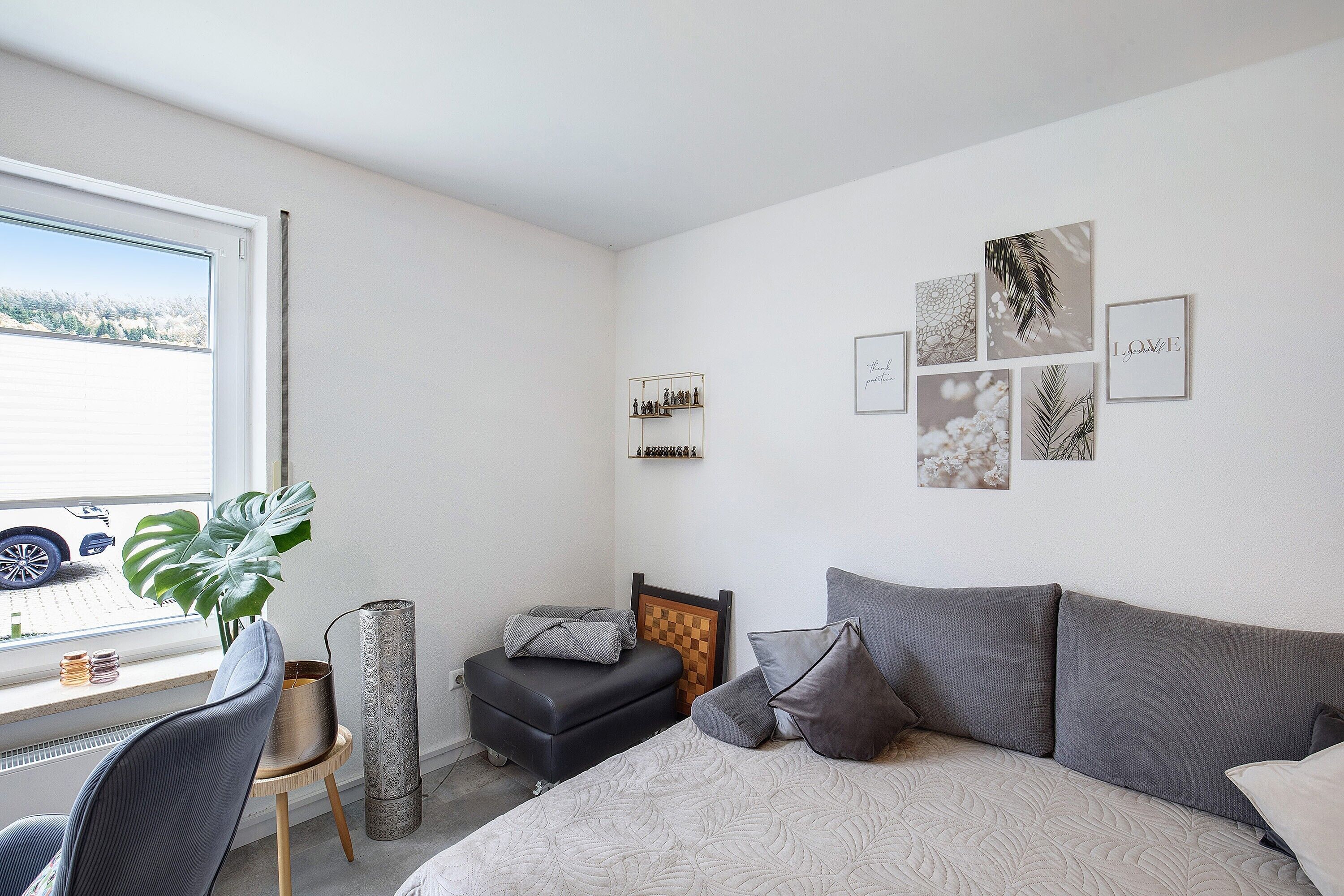 A bedroom with a bed, a desk, a chair, a potted plant, and artwork on the wall.
