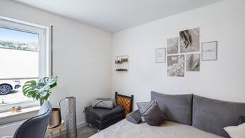 A bedroom with a bed, a desk, a chair, a potted plant, and artwork on the wall.