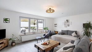 Een moderne woonkamer met een bank, een salontafel, een televisie en een raam met zonwering.