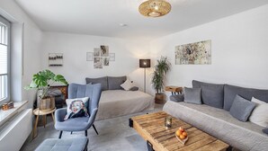 Een moderne woonkamer met een bank, fauteuil, bijzettafeltje en sierplanten.