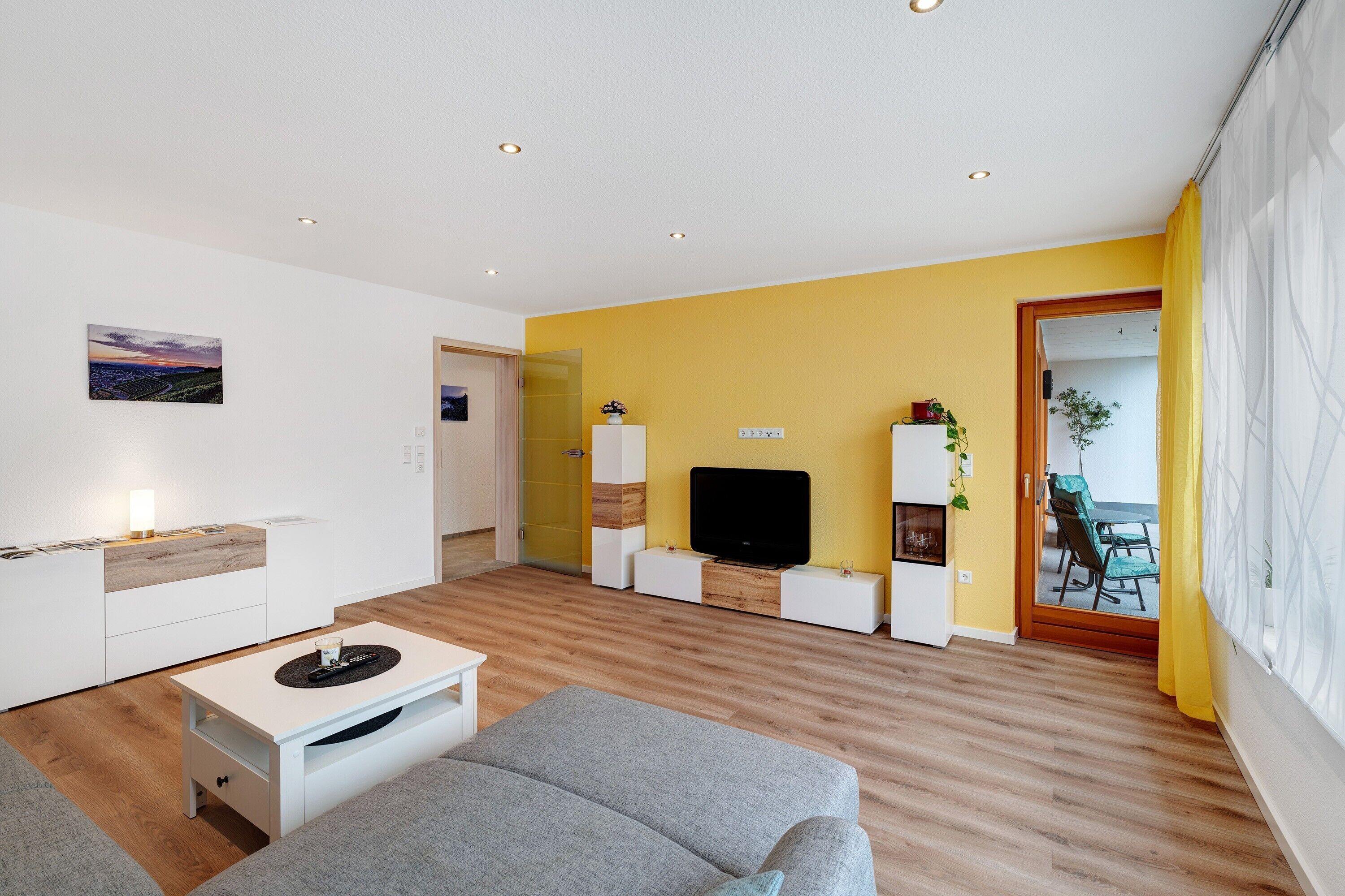 A modern living room with a sofa, a TV, and a dining area with yellow walls and wooden flooring.