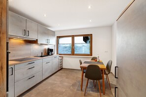 Eine moderne Küche mit Essbereich, ausgestattet mit hellen Holzschränken, einem eingebauten Ofen und einem Fenster mit Jalousien.