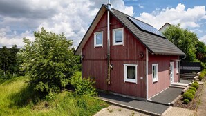 Un bâtiment rouge avec un toit en pente, deux fenêtres et une cheminée.