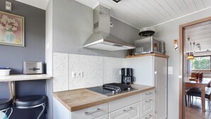 Une cuisine moderne équipée d’un four à micro-ondes, d’une cuisinière et d’une machine à café. On y trouve également un coin repas avec une table et des chaises, visibles à travers une porte vitrée.