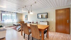 Un coin repas avec une table en bois, des chaises en osier, un luminaire suspendu, un miroir au mur et une porte en bois.