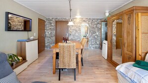 Une pièce comprenant une table à manger, des chaises, un canapé, un lit, un miroir et un mur en pierre.