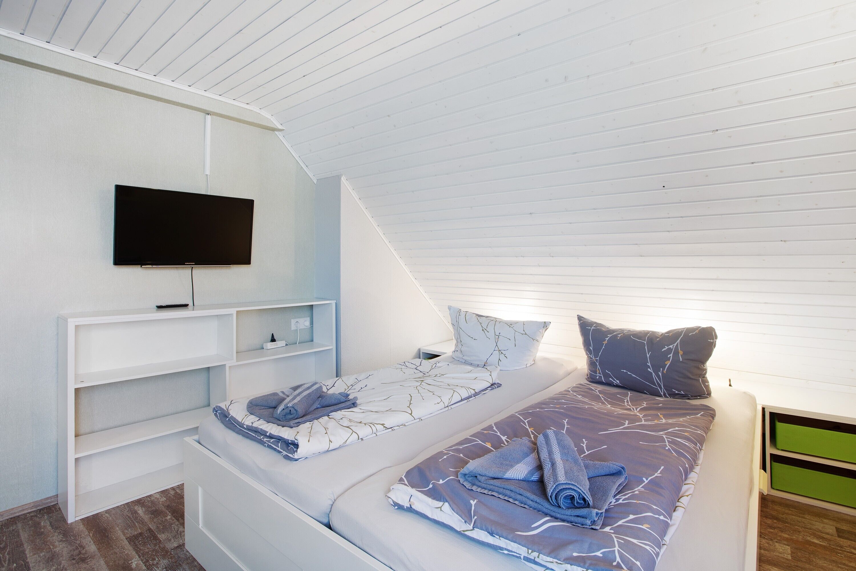 Un dormitorio con televisor montado en la pared, una cama con colcha estampada y techo blanco.