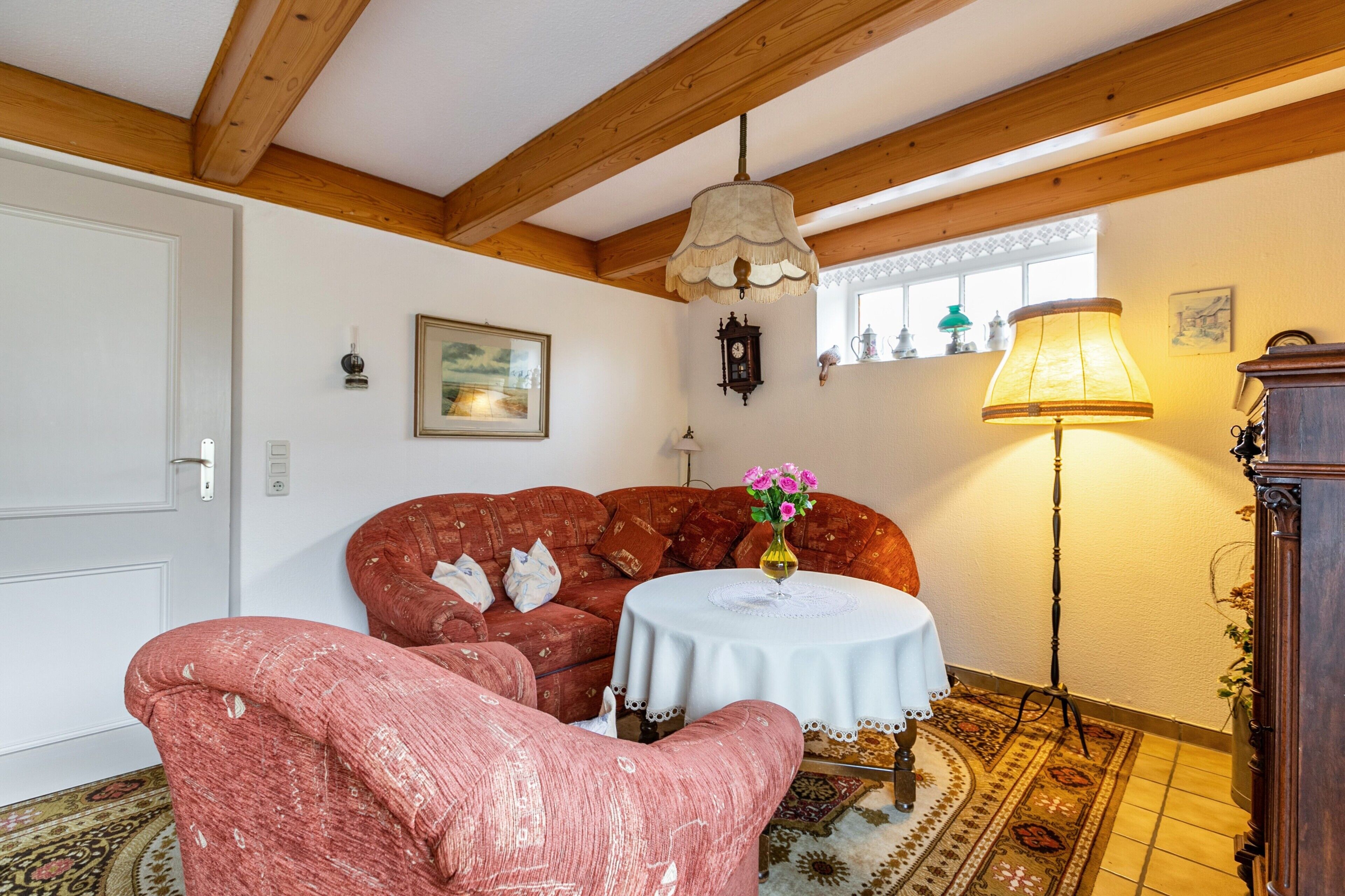 Une pièce avec un canapé rouge, une table blanche ornée d’un vase, un lampadaire et un plafond en bois.
