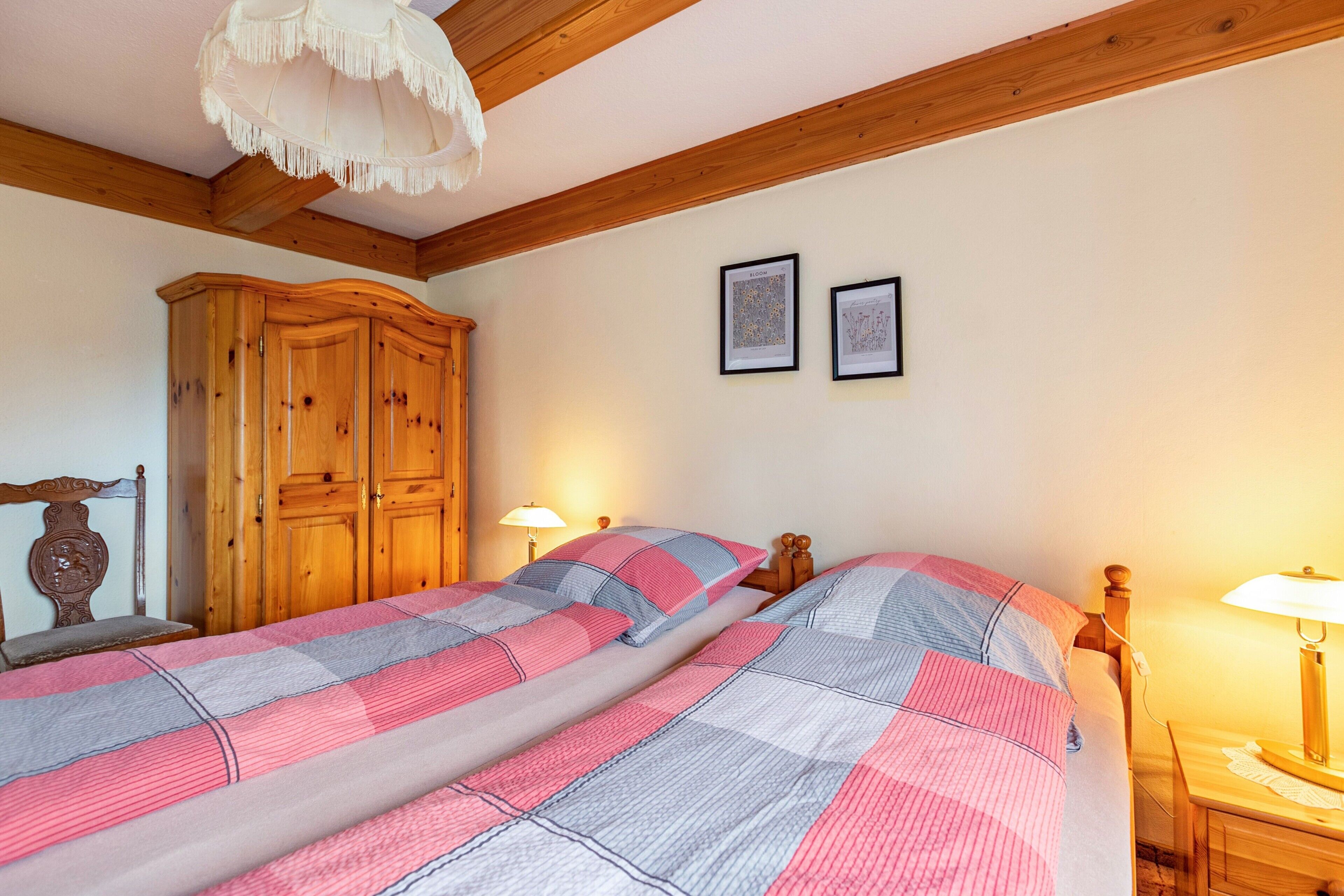 A bedroom with a wooden bed, two bedside tables, a wooden wardrobe, and a ceiling with exposed beams.