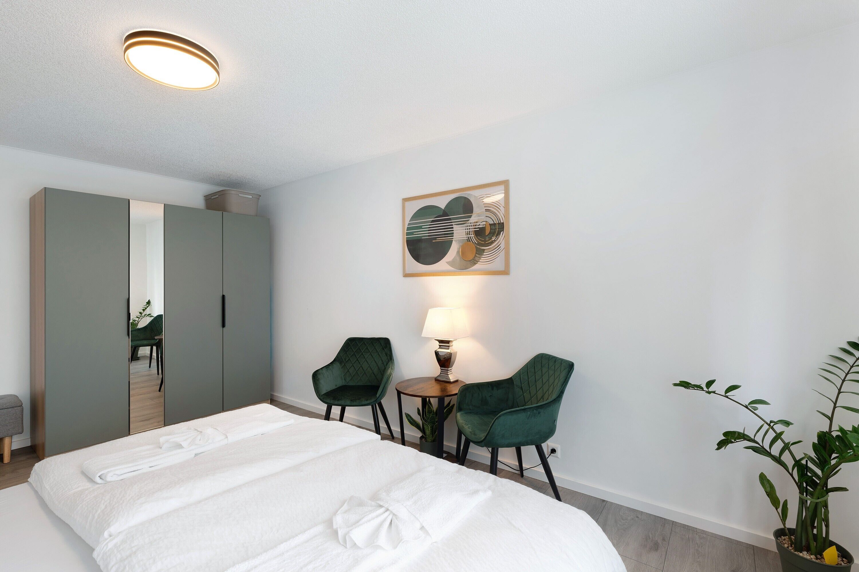 Een hotelkamer met een bed, twee stoelen, een tafel met een lamp, een spiegel en een inlijsting foto aan de muur.