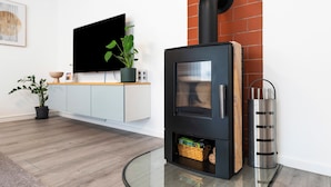 A modern living room with a black wood-burning stove, a flat-screen TV, a potted plant, and a wooden cabinet.