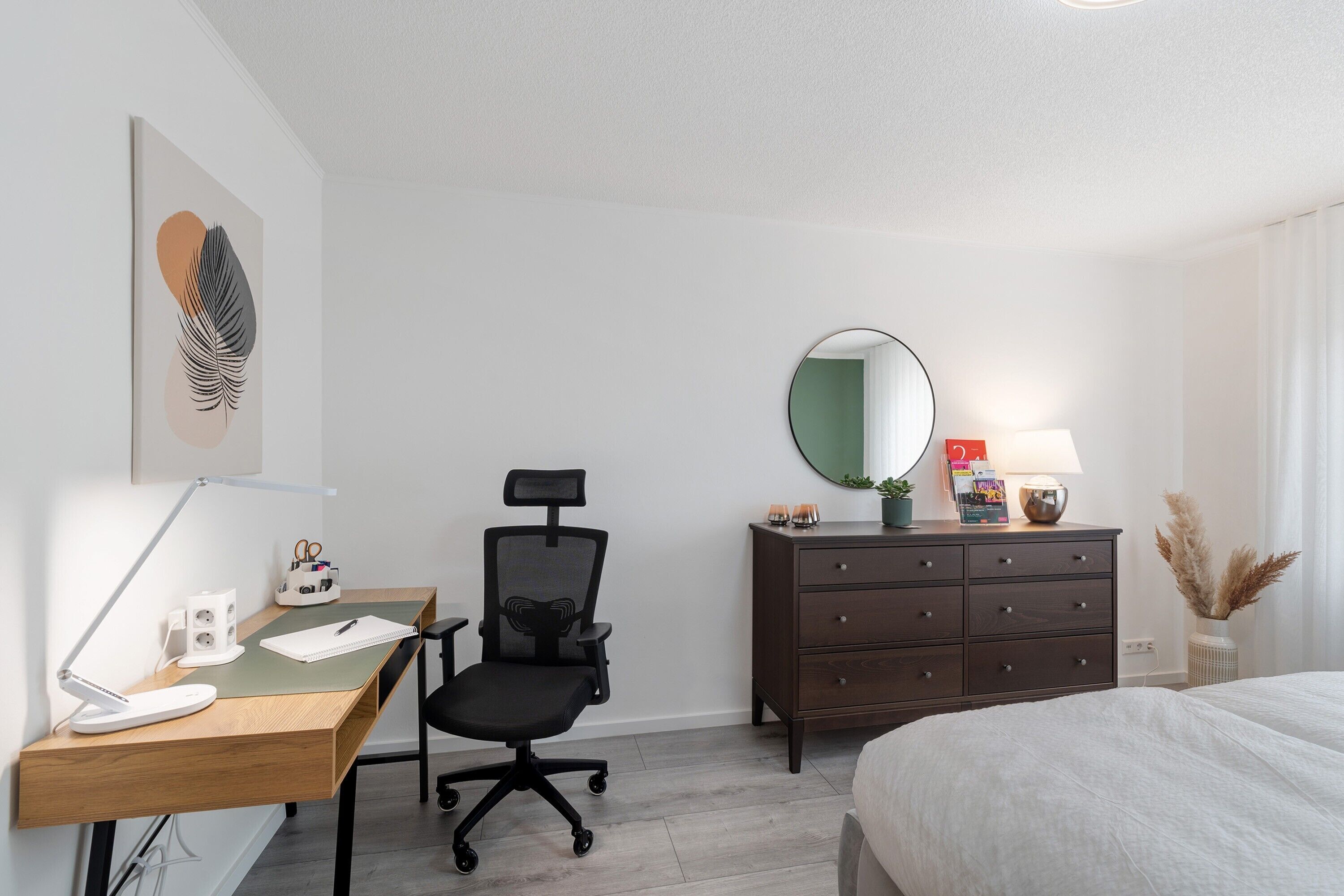 A hotel room with a desk, office chair, dresser, bed, and a mirror.