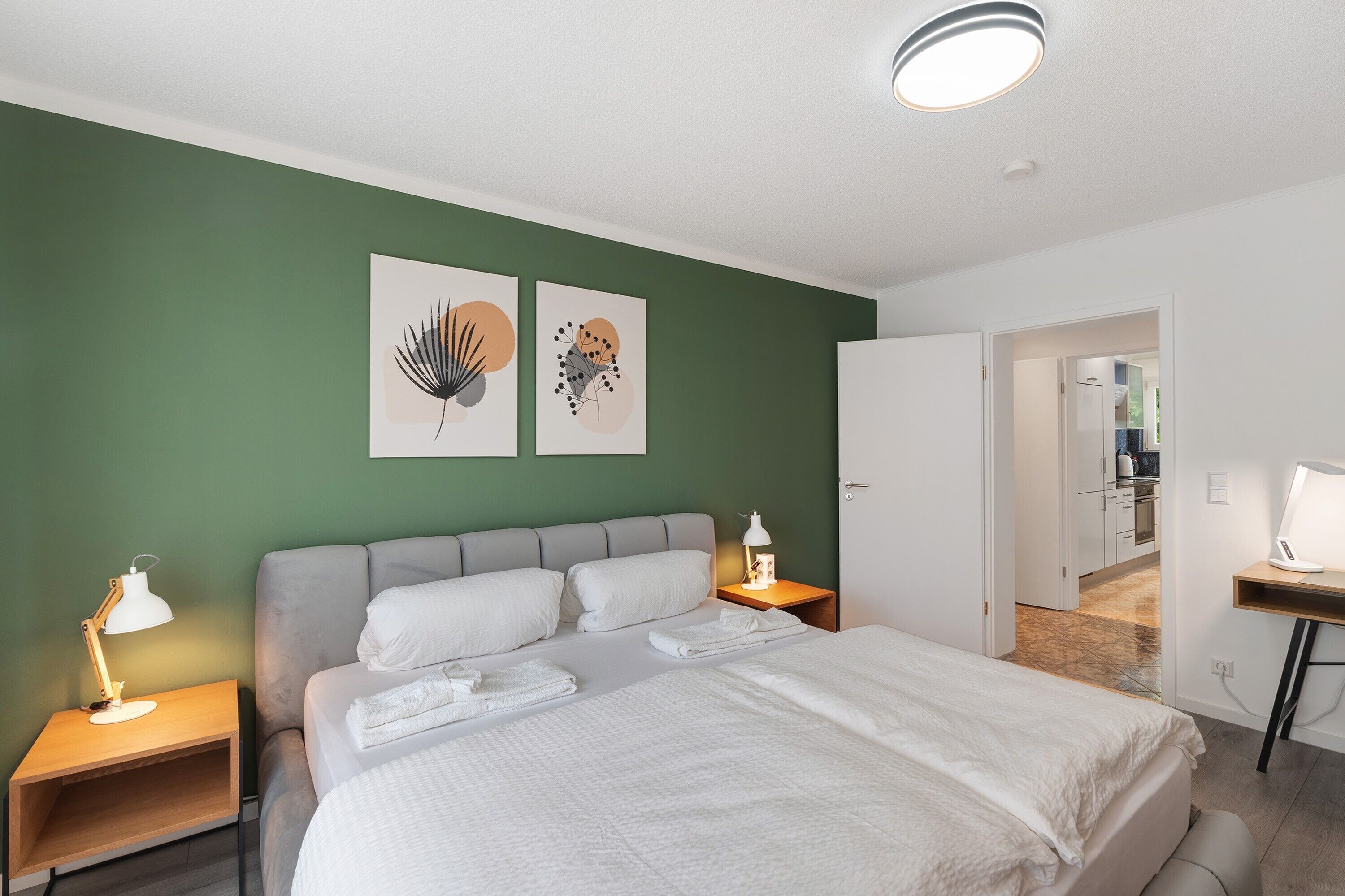 A neatly made bed with white linens, two bedside lamps, and artwork on the wall.