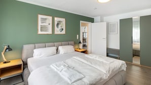 A modern hotel room with a large bed, a bedside table, a nightstand, and a wardrobe.