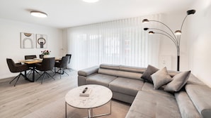 A modern living room with a sectional sofa, a dining table with chairs, and a coffee table.