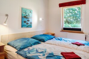 Een slaapkamer met twee bedden, een raam met uitzicht op bomen, een schilderij aan de muur en een bedlampje.