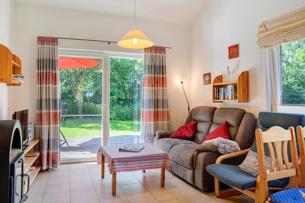 Een woonkamer met een bank, een houten stoel, een tafel, een boekenkast en een schuifdeur die uitkomt op een tuin.