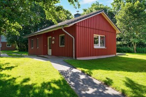 Een rode, gelijkvloerse woning met schuin dak, een voordeur en een klein voortuintje.