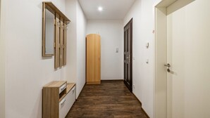 Um corredor com piso de madeira, um armário de madeira, um espelho, uma porta e um aparelho de iluminação.