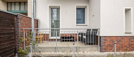 A covered outdoor area with a patio, a brick wall, and a metal fence.
