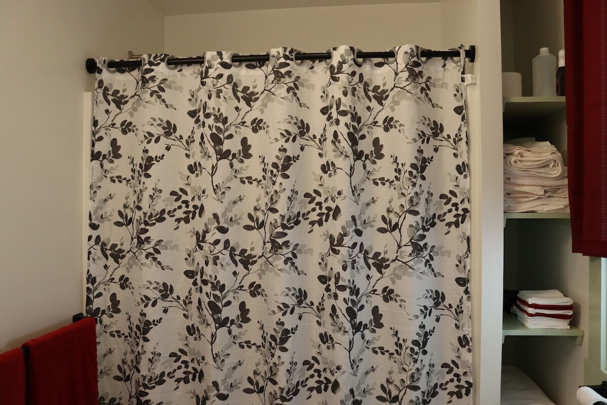 Une salle de bain avec un rideau de douche à motifs floraux, une serviette rouge et une étagère où sont pliées d’autres serviettes.