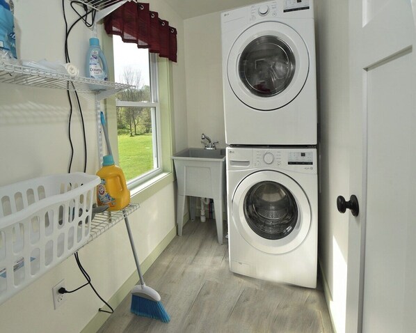 A laundry room with two stacked washing machines, a small sink, a broom, and a laundry basket.