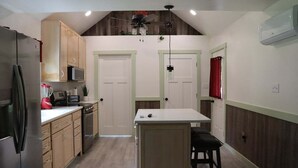Une cuisine de taille réduite, dotée de meubles en bois, d’un four à micro-ondes, d’un réfrigérateur et d’un ventilateur de plafond.