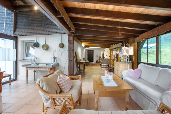 A spacious living area with a wooden ceiling, wicker furniture, a sofa, and a dining table.