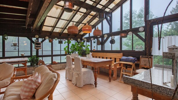 Een overdekt terras met rieten meubels, een houten tafel en hangende lampen.