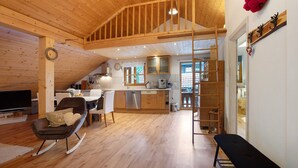 A spacious room with a wooden ceiling, a dining area, a kitchen, and a staircase leading to an upper level.